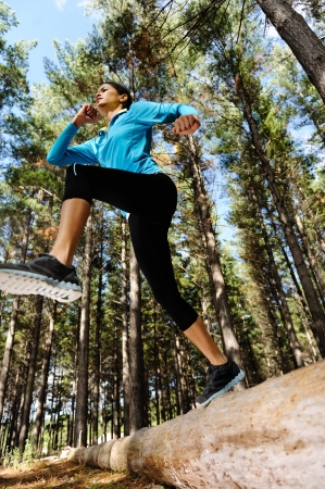 Woman trail running in the woods and jumping over logs while on extreme outdoor fitness training in forest  の写真素材