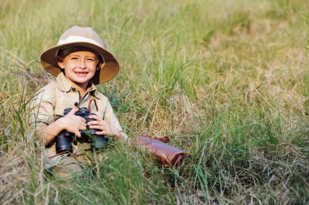 Young boy child playing pretend explorer adventure safari game outdoors with binoculars and bush hatの写真素材