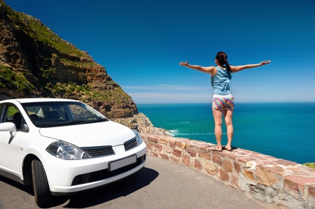 carefree tourist stands on chapmans peak drive with arms outstretched in freedom girl pose with rental carの写真素材