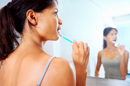 Portrait of attractive woman brushing teeth in bathroom and looking in the mirror at reflectionの写真素材