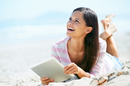 carefree woman uses touchpad tablet technology on the beach with internet vacationの写真素材