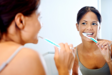 Portrait of attractive woman brushing teeth in bathroom and looking in the mirror at reflection. healthy teeth.の写真素材