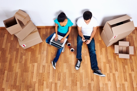 overhead view of couple sitting on floor together using computer wireless internet while moving into new homeの写真素材