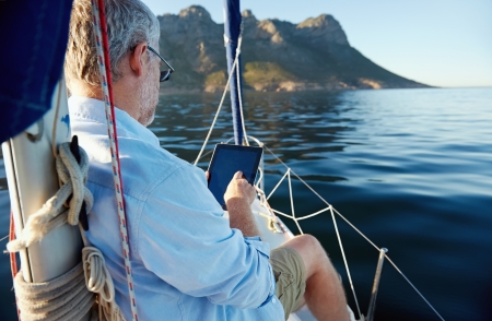sailing man reading tablet computer on boat with modern technology and carefree retired senior successful lifestyleの写真素材