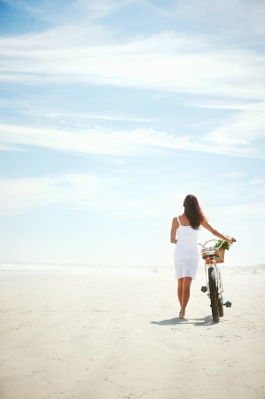 Woman walking with bicycle along beach sand summer lifestyle carefreeの写真素材