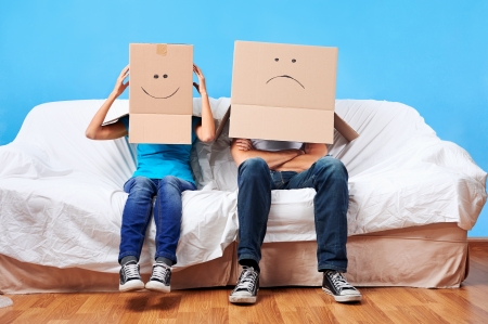 couple sitting on couch with moving boxes on head having fun togetherの写真素材