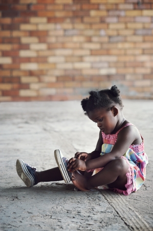 Young african girl tying shoelace and putting shoot on foot in rural settingの写真素材