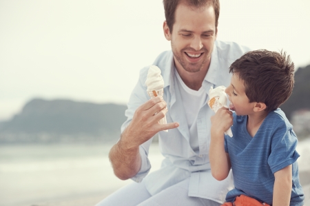Father and son eating icecream together at the beach on vacation having fun with melting messの写真素材