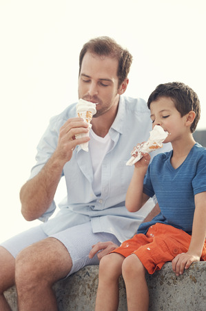 Father and son eating icecream together at the beach on vacation having fun with melting messの写真素材