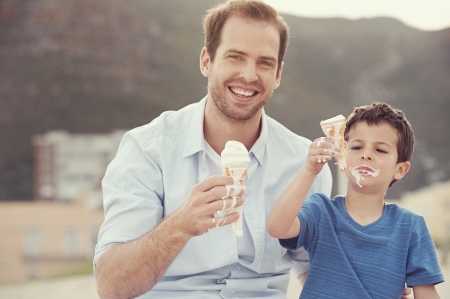 Father and son eating icecream together at the beach on vacation having fun with melting messの写真素材
