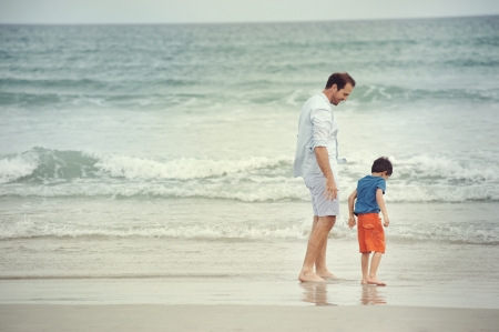 Father and son at beach holding hands looking at the ocean together on vacationの写真素材
