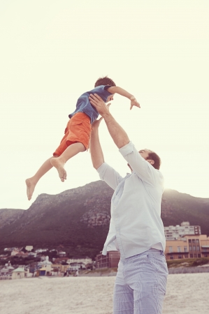 Father throwing son in air at beach having fun playful laughing dadの写真素材