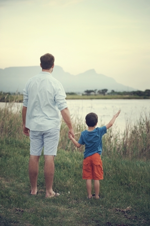 Father and son holding hands looking out over the lake at the mountain at sunsetの写真素材