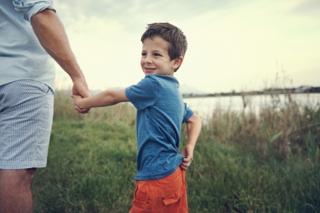 little boy holding hands with dad and smiling over his shoulderの写真素材