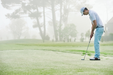 Golf man putting on green and aiming to sink golf putt shot on course