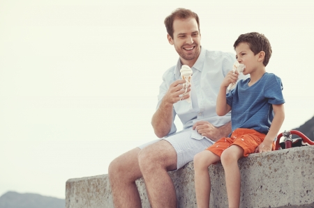 Father and son eating icecream together at the beach on vacation having fun with melting messの写真素材