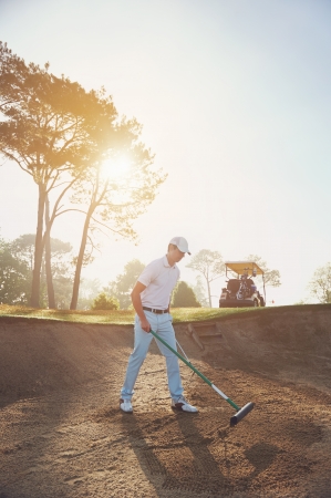 Golfer raking bunker in early morning with sunriseの写真素材
