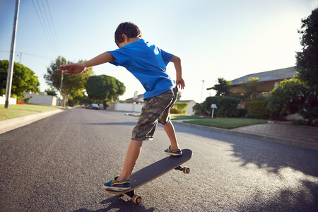 young boy learning to ride skateboard in the suburb street having fun.の写真素材