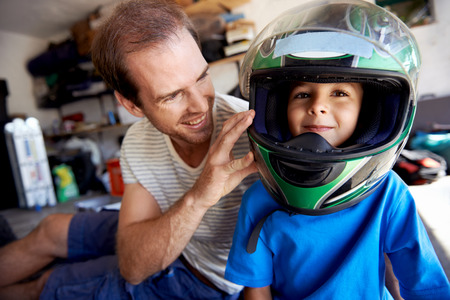 portrait of young boy playing with fathers motorbike helmet and helping his dad with fixing a motorcycle in the garageの写真素材