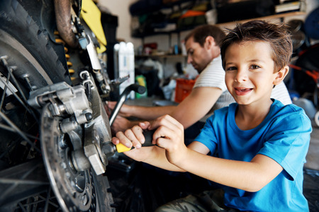 portrait of a boy helping his dad with fixing a motorcycle in the garageの写真素材