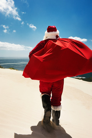 Back-view of Santa Claus walking along a beach holding a sack full of presentsの写真素材
