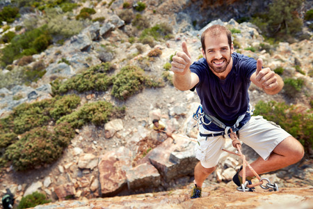 A rockclimber with rockclimbing equipment on holding a thumbs up and smiling at  the cameraの写真素材