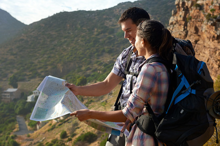 Smiling couple with backpacks on hiking trail looking at map