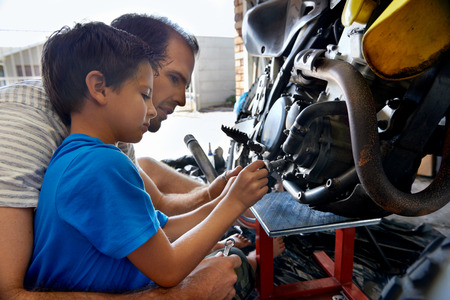 A boy helping his dad with fixing a motorcycle in the garageの写真素材