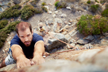 A man holding on to a piece of rock while he climbs up a steep cliff with copyspaceの写真素材