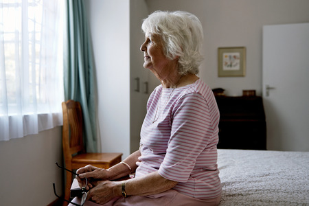 A solemn elderly woman sitting on her bed dealing with depressionの写真素材