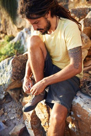 Hiker with dreadlocks tying his shoelaces on a mountainの写真素材