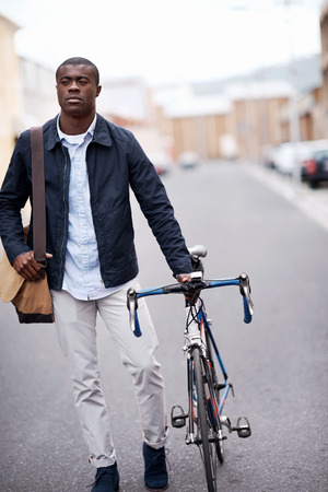 young trendy black african hipster man with bicycle walking in urban city on way commute to workの写真素材