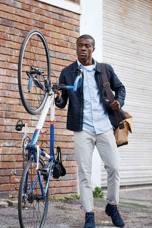 young trendy black african hipster man with bicycle walking in urban city on way commute to workの写真素材