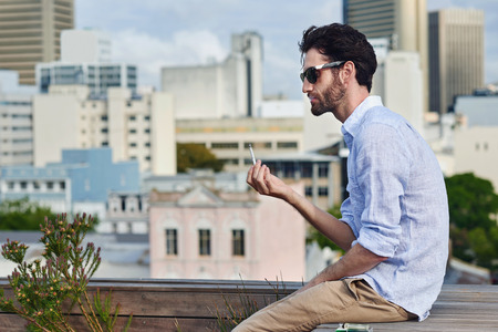 Young man sitting outdoors smoking a cigarette on the rooftop terrace in cityの写真素材
