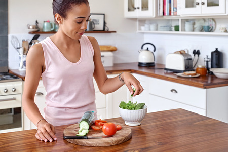 young woman making tomato cucumber salad bowl kitchen at homeの写真素材