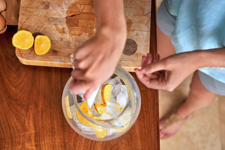 Woman putting ice and lemon in jug for a refreshing drink in kitchenの写真素材