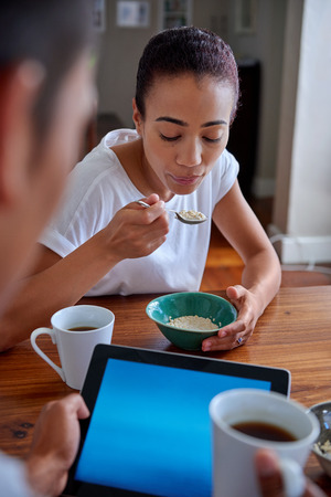 couple enjoying a healthy morning breakfast cereal with tablet computer in kitchen at homeの写真素材