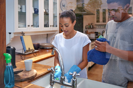 candid image of young woman washing dirty dishes while husband dry off in kitchenの写真素材