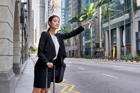 traveling asian chinese business woman calling for taxi cab from city street sidewalkの写真素材