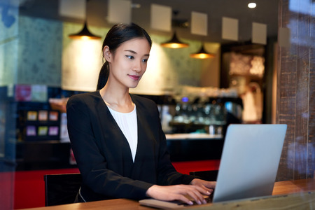 young asian chinese business woman using cafe wifi connection for laptop computer workの写真素材