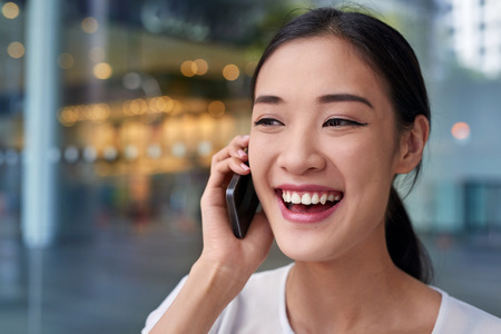 happy asian chinese business woman talking on mobile cell phone at workの写真素材