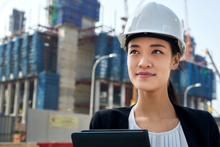 professional asian chinese business woman supervising construction site with hard hat protection at workの写真素材
