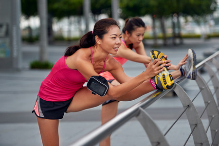 athletic asian chinese women doing stretching exercises outdoors along city sidewalk