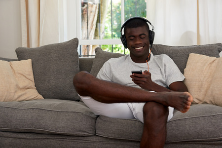 happy mobile cellphone african black man listening music sofa couch at home living roomの写真素材