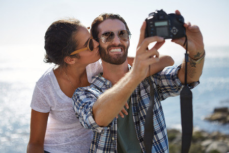 happy couple take a selfie with a kiss, with a beautiful ocean background using a digital cameraの写真素材