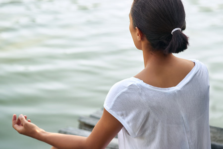 Rear view of young woman in a yoga position near a lake, pondの写真素材