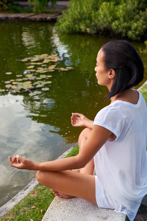 yound female sitting near a pond, lake in a yoga positionの写真素材