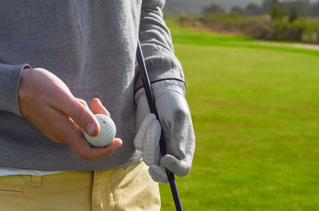 golfing man holding golf ball and club outdoorsの写真素材