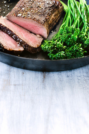 Medium cooked steak on a cast iron pan with fresh green vegetablesの写真素材