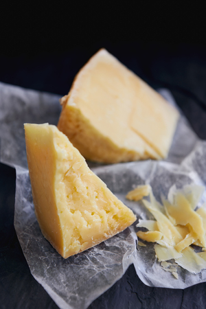 Block of mature hard cheese, broken into blocks, sliced on the side served on waxed paper and slateの写真素材